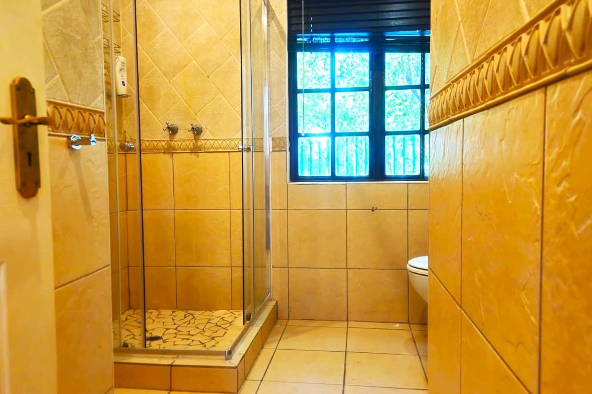 A bathroom featuring a glass shower enclosure, tiled walls and flooring, and a toilet, with natural light provided by a window.