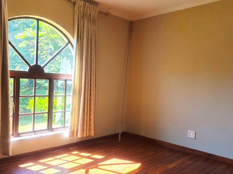 A bright, empty bedroom featuring warm laminate flooring and a distinctive arched window that allows for ample natural light.