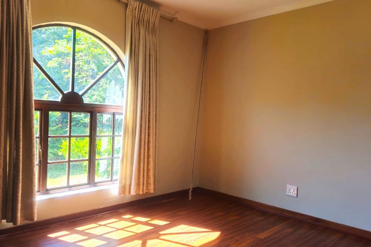 A bright, empty bedroom featuring warm laminate flooring and a distinctive arched window that allows for ample natural light.