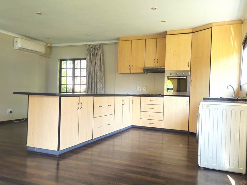 Open-plan kitchen and living area featuring light wood cabinetry, built-in oven, laminate flooring, and a split-system air conditioner.