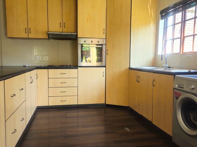 A functional kitchen featuring light wood-tone cabinetry, dark laminate countertops, built-in oven, extractor fan, and a stainless steel sink with a window view.