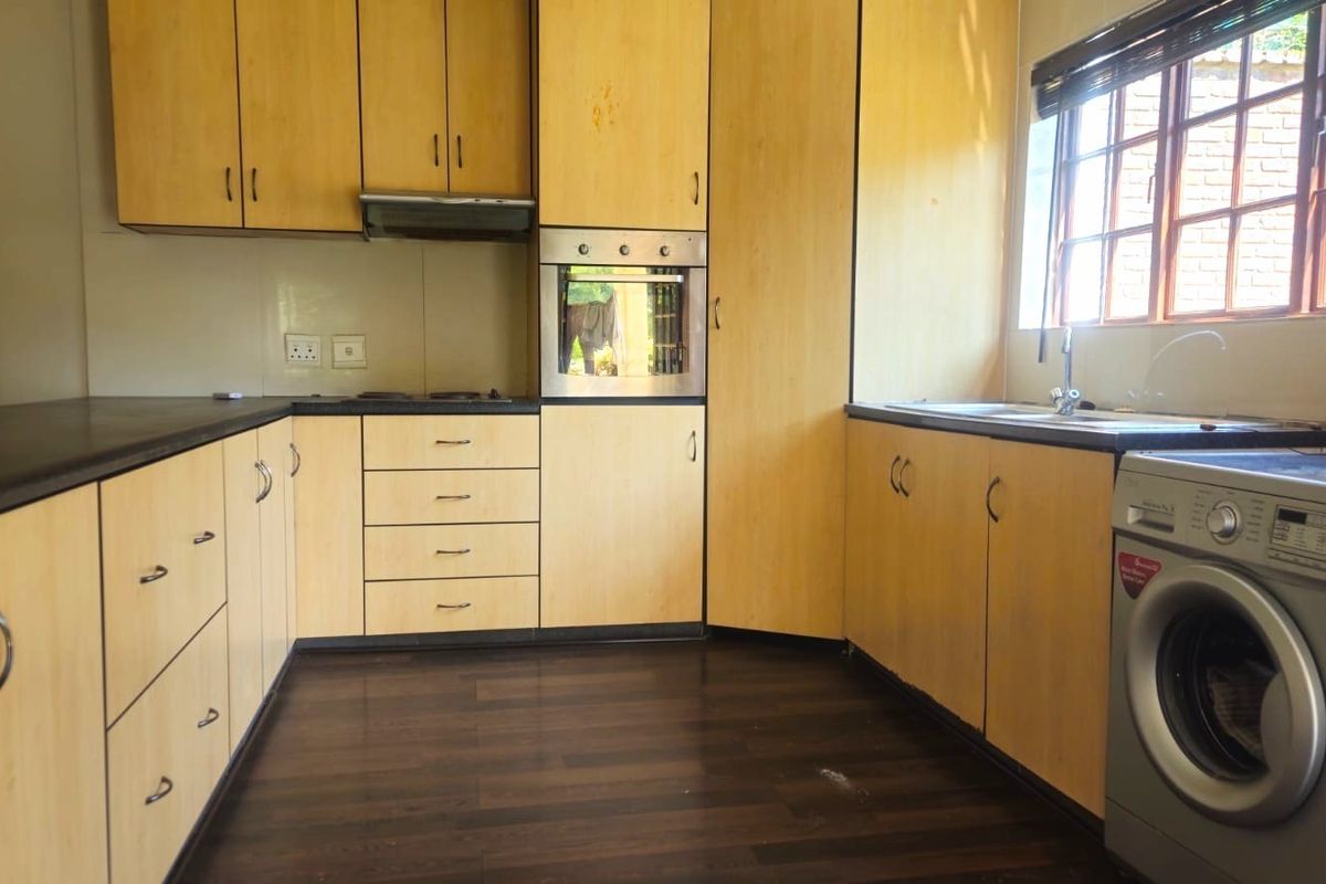 A functional kitchen featuring light wood-tone cabinetry, dark laminate countertops, built-in oven, extractor fan, and a stainless steel sink with a window view.