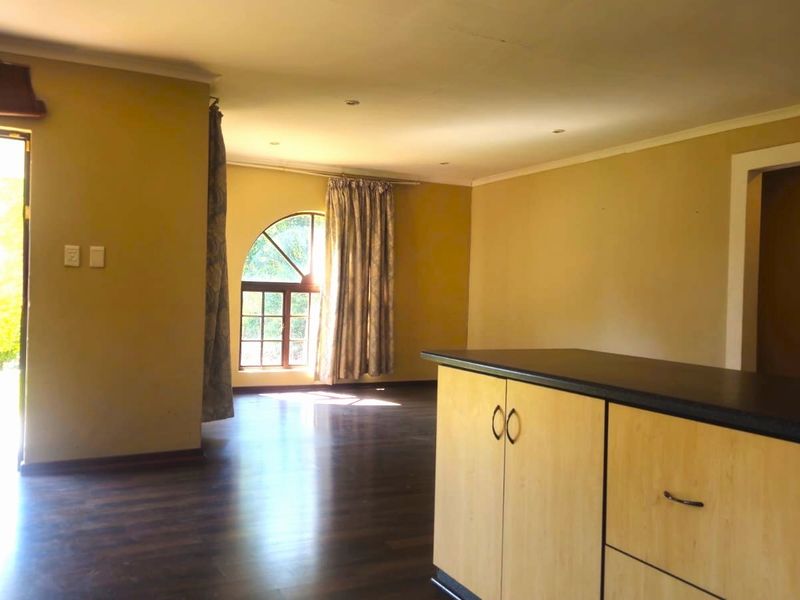 Spacious open-plan living area featuring dark laminate flooring, an arched window, and a functional kitchen island with built-in cabinetry.