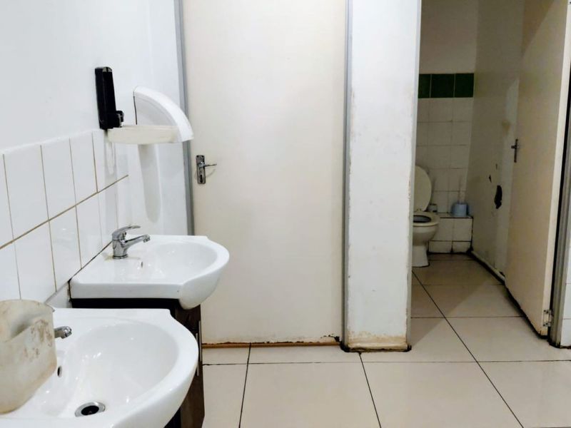 Commercial bathroom facility featuring dual washbasins, tiled walls and flooring, and a separate toilet cubicle with visible wear and tear.