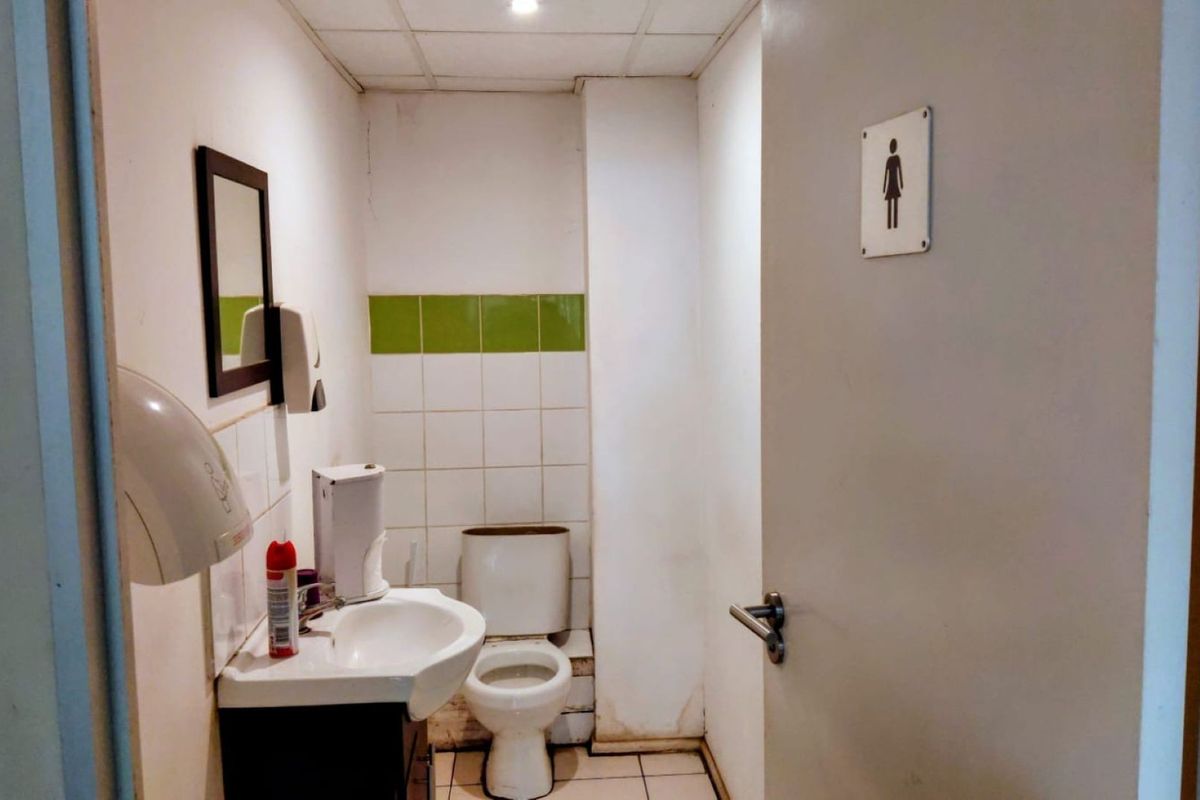 A functional commercial restroom featuring a toilet, washbasin, wall-mounted hand dryer, and tiled splashback, requiring cosmetic updates to improve its overall condition.