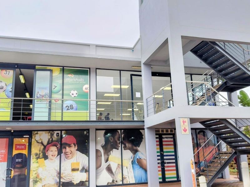 A modern commercial building exterior featuring a prominent metal staircase, glass storefronts, and large promotional window graphics.