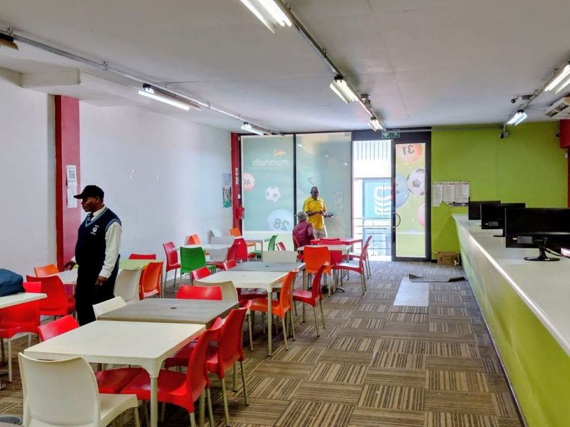 Open-plan commercial betting shop interior featuring a long service counter, fluorescent lighting, and carpeted flooring with multiple seating areas.