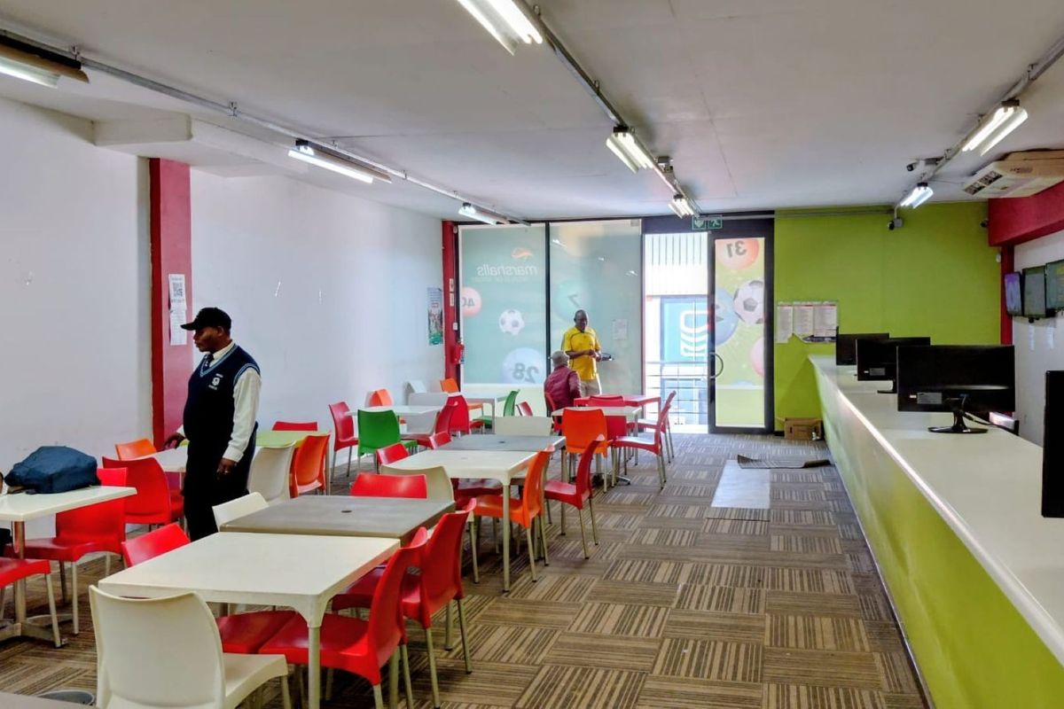 Open-plan commercial betting shop interior featuring a long service counter, fluorescent lighting, and carpeted flooring with multiple seating areas.