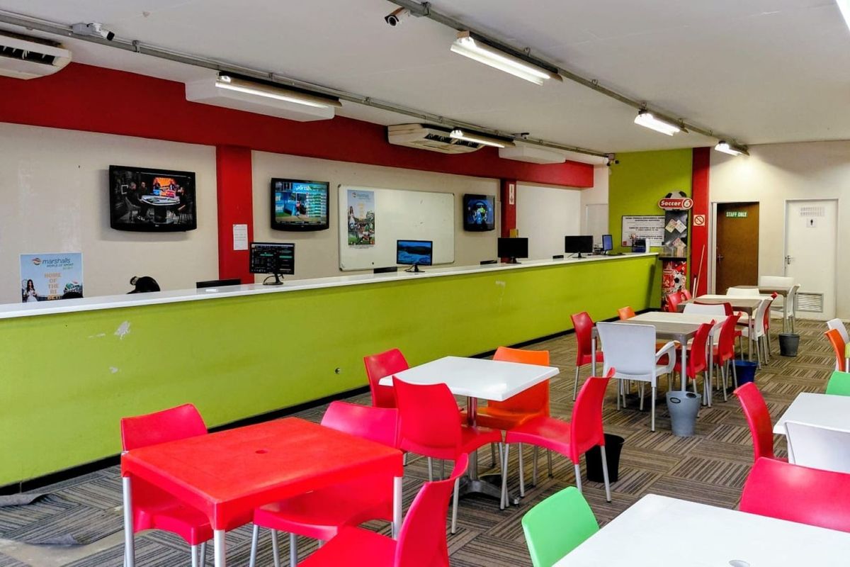 Open-plan commercial betting or service area featuring a long service counter, fluorescent lighting, air conditioning, and carpeted flooring.