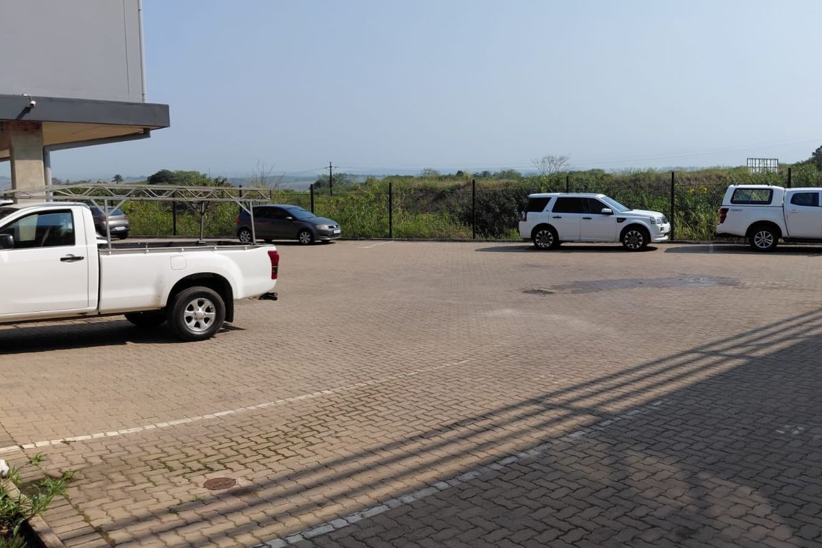 An industrial exterior view featuring a paved parking area with perimeter fencing and a concrete building overhang.