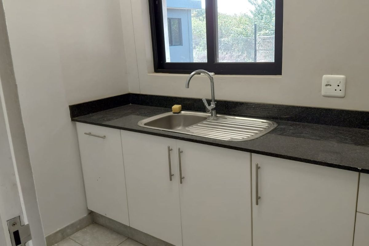 A clean, functional kitchen area featuring white built-in cabinetry, a dark granite countertop, and a stainless steel sink with a modern faucet.