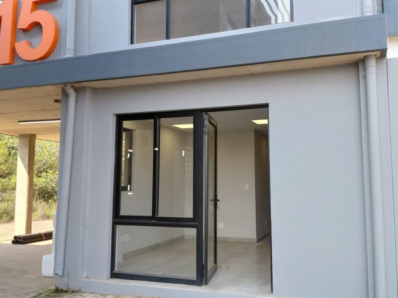 Modern industrial unit entrance featuring a sleek aluminium-framed glass door, large window, and clean grey facade with contemporary recessed lighting.