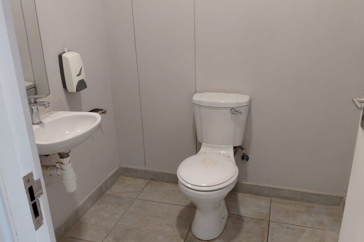 A functional industrial-style restroom featuring a wall-mounted basin, standard toilet, and tiled flooring.