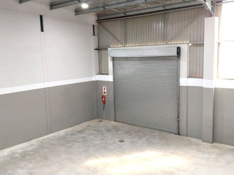 A clean, functional industrial utility space featuring concrete flooring, high ceilings with exposed steel structure, and a secure roller shutter door.
