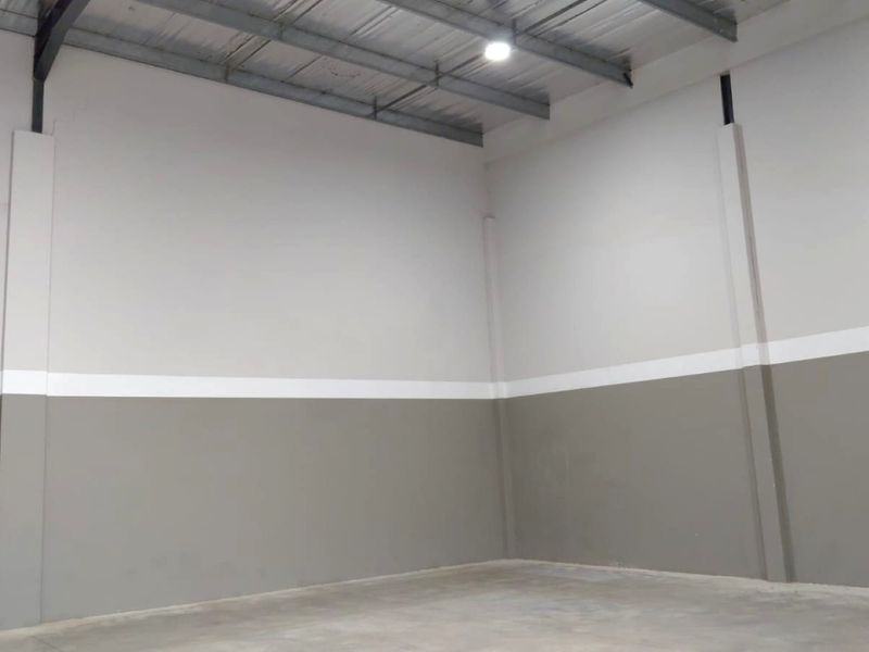 A clean, empty industrial utility space featuring exposed steel roof trusses, concrete flooring, and freshly painted masonry walls with industrial lighting.