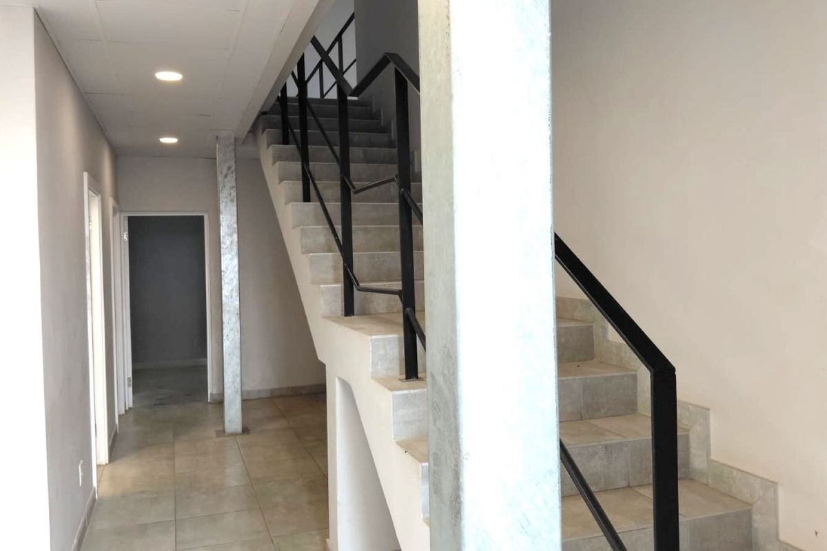 A clean, modern hallway featuring a tiled staircase with a black metal handrail, recessed lighting, and neutral finishes throughout the industrial space.