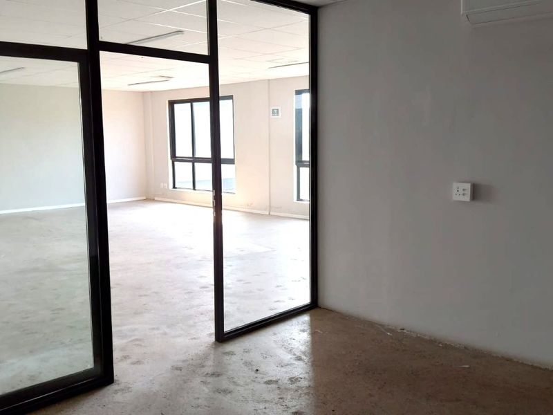 An open-plan office space featuring a glass partition, suspended ceiling, and air conditioning unit, with polished concrete flooring throughout.