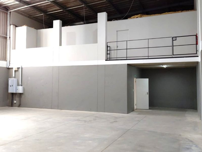 Spacious industrial warehouse unit featuring a concrete floor, high ceilings with exposed steel structure, and a functional mezzanine level with safety railing.