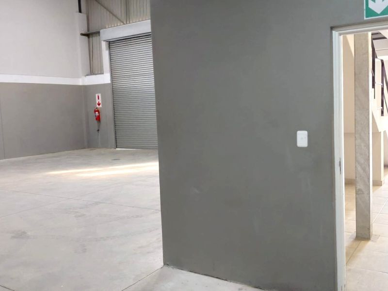 Spacious industrial warehouse unit featuring concrete flooring, a large roller shutter door, and an adjacent staircase leading to an upper level.