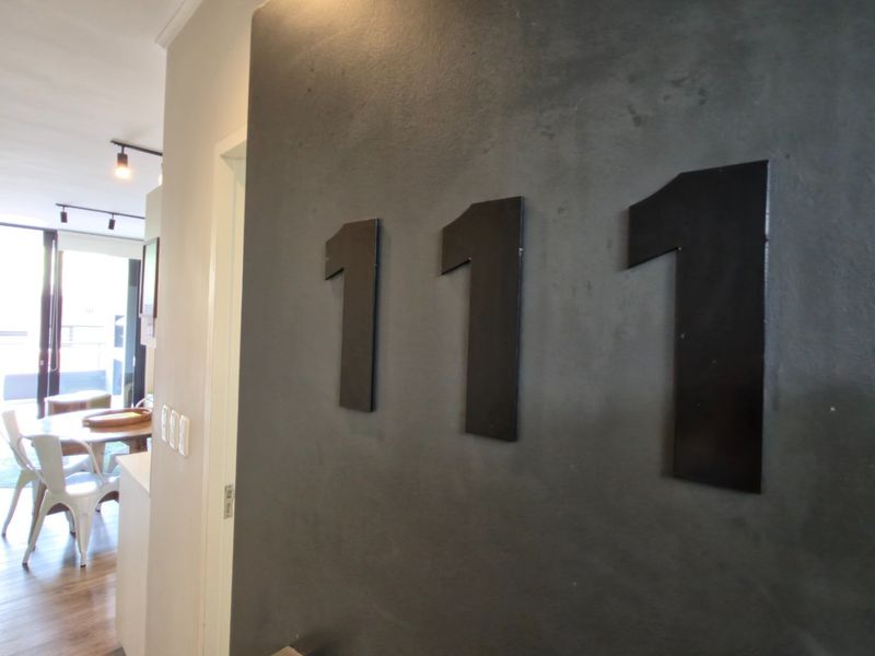 Entryway featuring a dark accent wall with apartment number signage, leading into an open-plan living area with laminate flooring and track lighting.