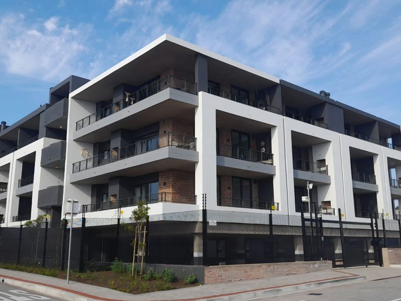 Modern multi-story apartment complex featuring contemporary architectural design, private balconies, and secure perimeter fencing in a well-maintained urban setting.