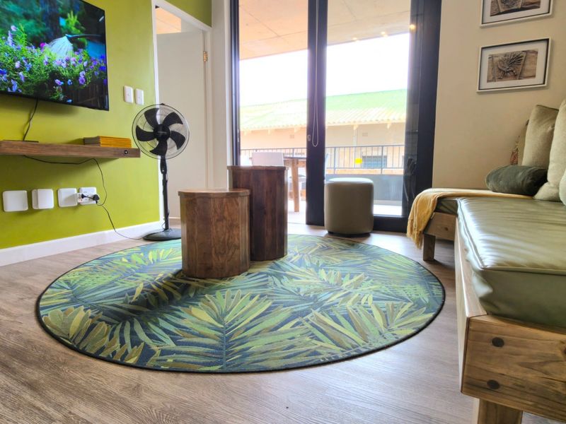 A bright living room featuring laminate flooring, a floating media shelf, and large sliding glass doors providing access to an outdoor balcony area.