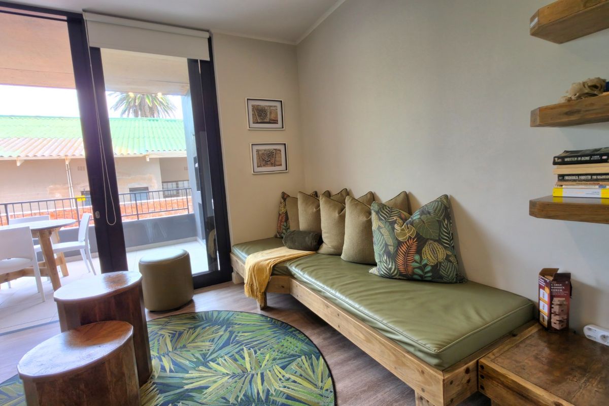 A cozy living area featuring laminate flooring, floating wooden shelves, and a large sliding glass door providing access to an outdoor balcony.