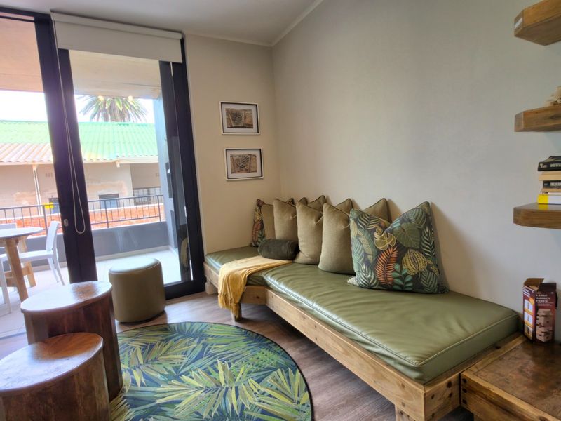 A cozy living area featuring laminate flooring, floating wooden shelves, and a large sliding glass door providing access to an outdoor balcony.