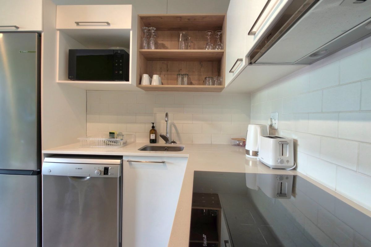 Modern kitchen featuring white cabinetry, subway tile backsplash, stone countertops, integrated dishwasher, induction cooktop, and stainless steel appliances.