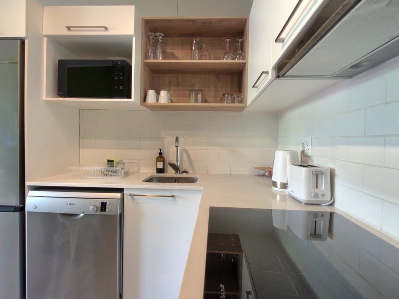 Modern kitchen featuring white cabinetry, subway tile backsplash, stone countertops, integrated dishwasher, induction cooktop, and stainless steel appliances.