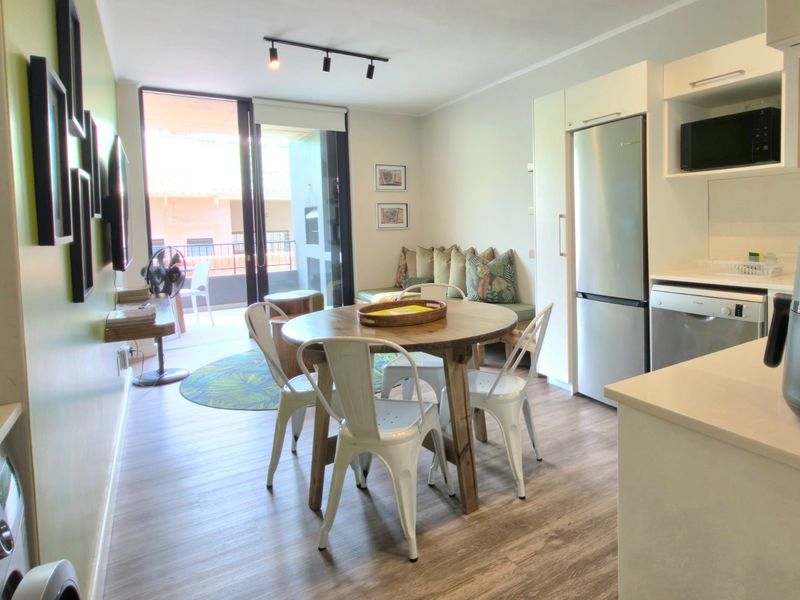 Open-plan living and dining area featuring modern cabinetry, stone countertops, integrated appliances, and direct access to a private balcony through sliding glass doors.