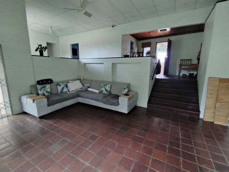 Spacious living area featuring terracotta tile flooring, a built-in brick partition, and a staircase leading to an elevated section with timber ceilings.