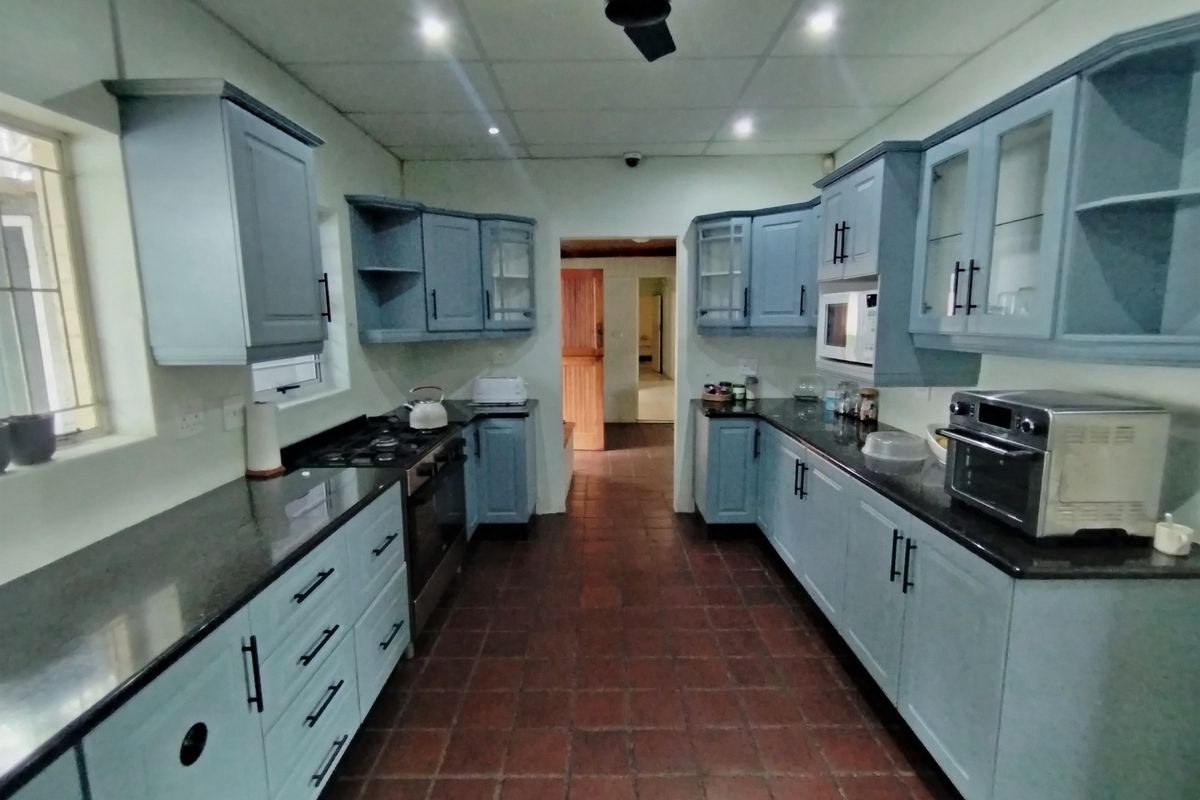 A functional kitchen featuring blue cabinetry, granite countertops, a gas hob, and built-in oven, with tiled flooring and recessed ceiling lighting.