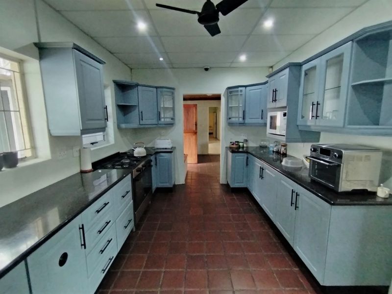 A functional kitchen featuring blue cabinetry, granite countertops, a gas hob, and built-in oven, with tiled flooring and recessed ceiling lighting.