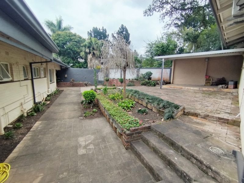 Rear courtyard featuring a paved patio, covered outdoor area, and raised brick garden beds, offering a functional space for outdoor living and landscaping.