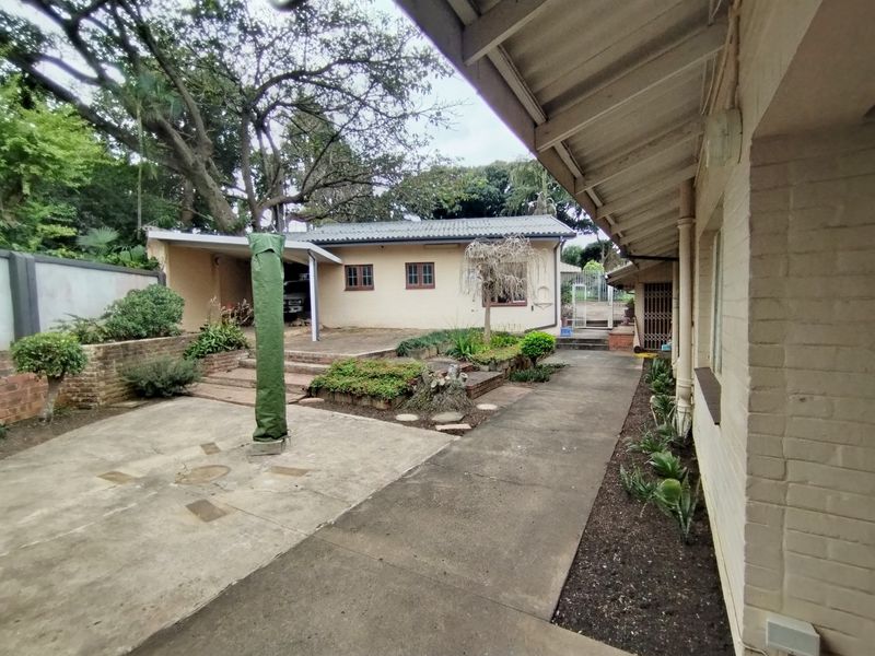 Rear exterior view featuring a concrete patio area, brick retaining walls, and a covered walkway along the side of the house.