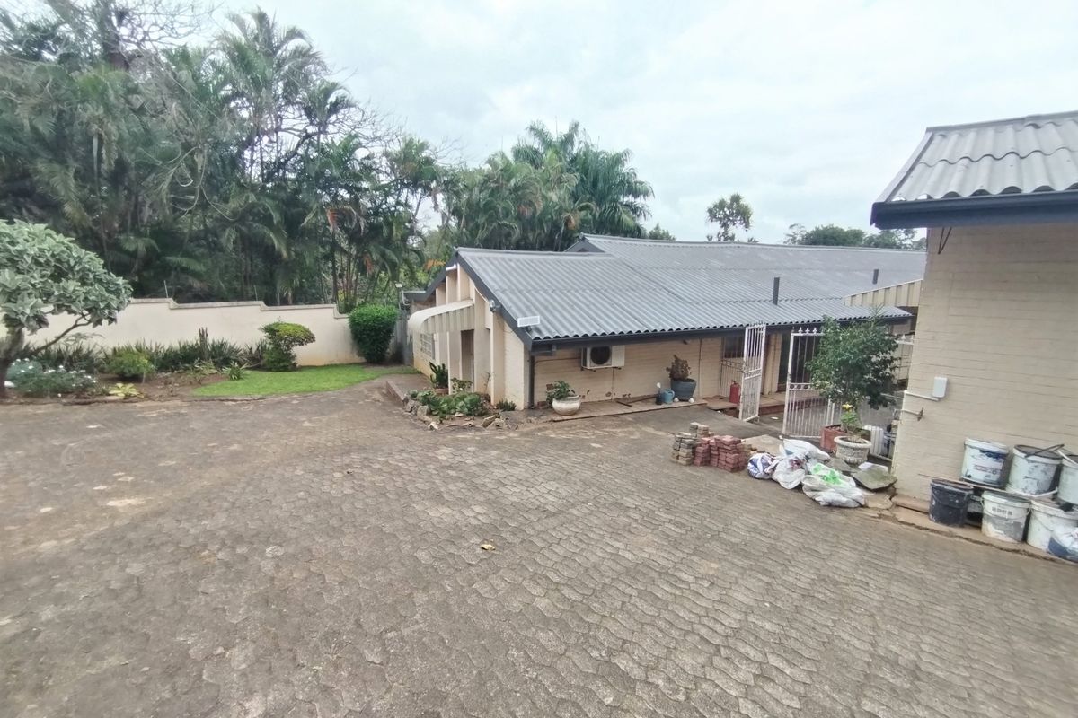 Rear exterior view of the property featuring a large brick-paved driveway, corrugated metal roofing, and a perimeter boundary wall.