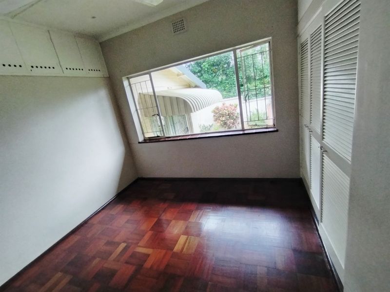 An empty bedroom featuring classic parquet flooring, built-in louvered cupboards, and overhead storage units, offering a blank canvas for personalization.