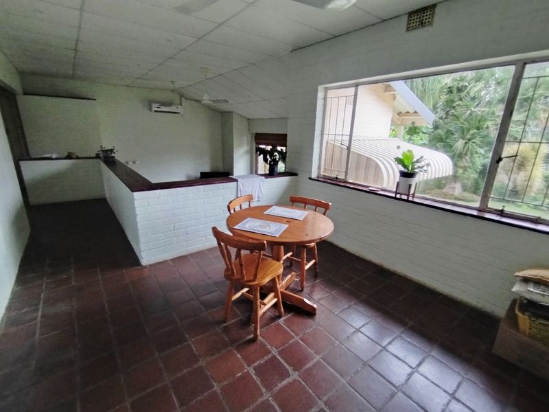 Living area featuring terracotta tile flooring, a brick half-wall partition, and a split-system air conditioner, with large windows overlooking the garden.