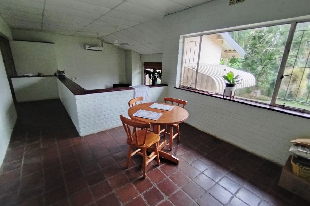 Living area featuring terracotta tile flooring, a brick half-wall partition, and a split-system air conditioner, with large windows overlooking the garden.