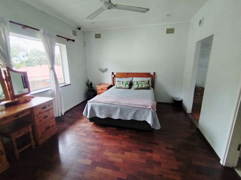 Spacious bedroom featuring warm parquet flooring, a ceiling fan, and natural light through a large window.