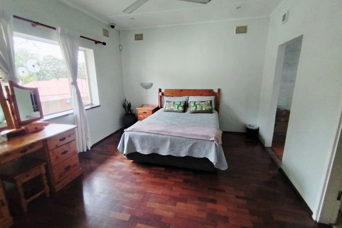 Spacious bedroom featuring warm parquet flooring, a ceiling fan, and natural light through a large window.