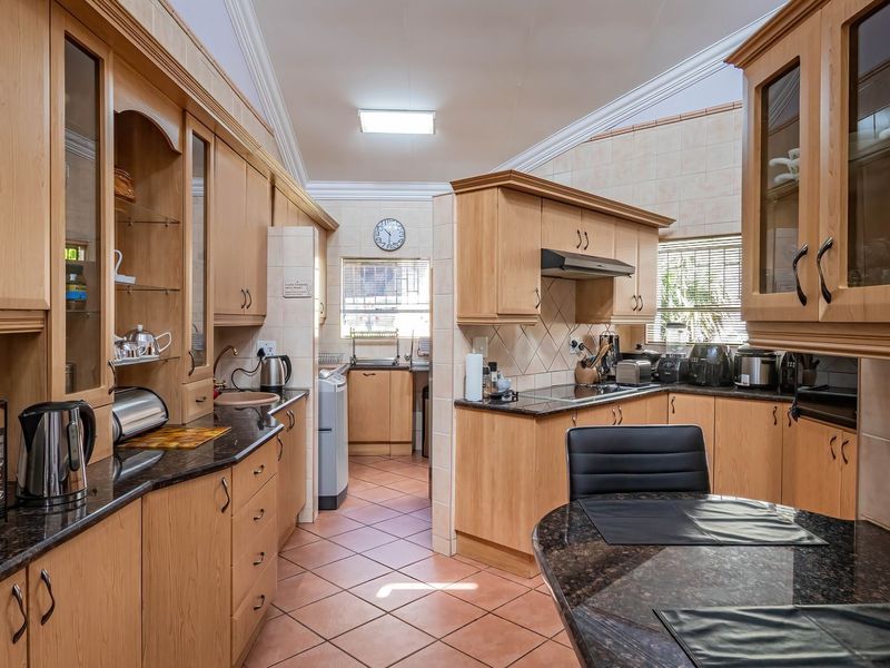 A spacious kitchen featuring light wood cabinetry, dark granite countertops, tiled flooring, and a functional layout with a separate scullery area.