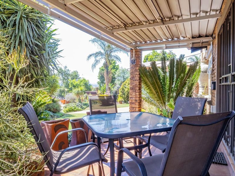 A covered outdoor patio area featuring tiled flooring, a brick support pillar, and direct access to the garden.