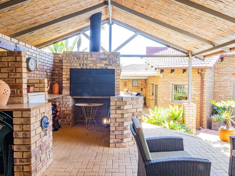 Covered outdoor patio featuring a built-in brick braai, exposed steel rafters, and brick paving, providing a functional space for outdoor entertaining.