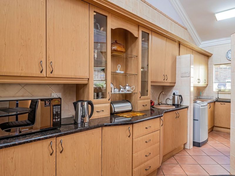 A functional kitchen featuring extensive wooden cabinetry, granite countertops, tiled backsplash, and tiled flooring, offering ample storage and workspace.