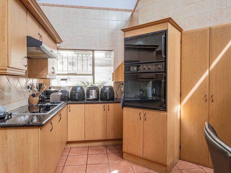 A functional kitchen featuring light wood cabinetry, dark laminate countertops, a built-in double oven, electric cooktop, and ceramic tile finishes throughout.