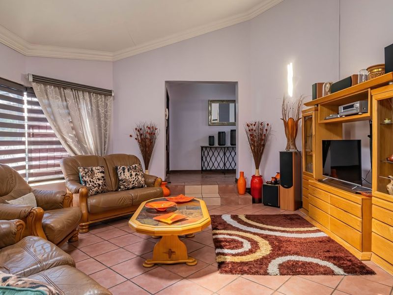 A spacious living room featuring tiled flooring, coved ceilings, and a stepped transition leading to an adjacent hallway area.