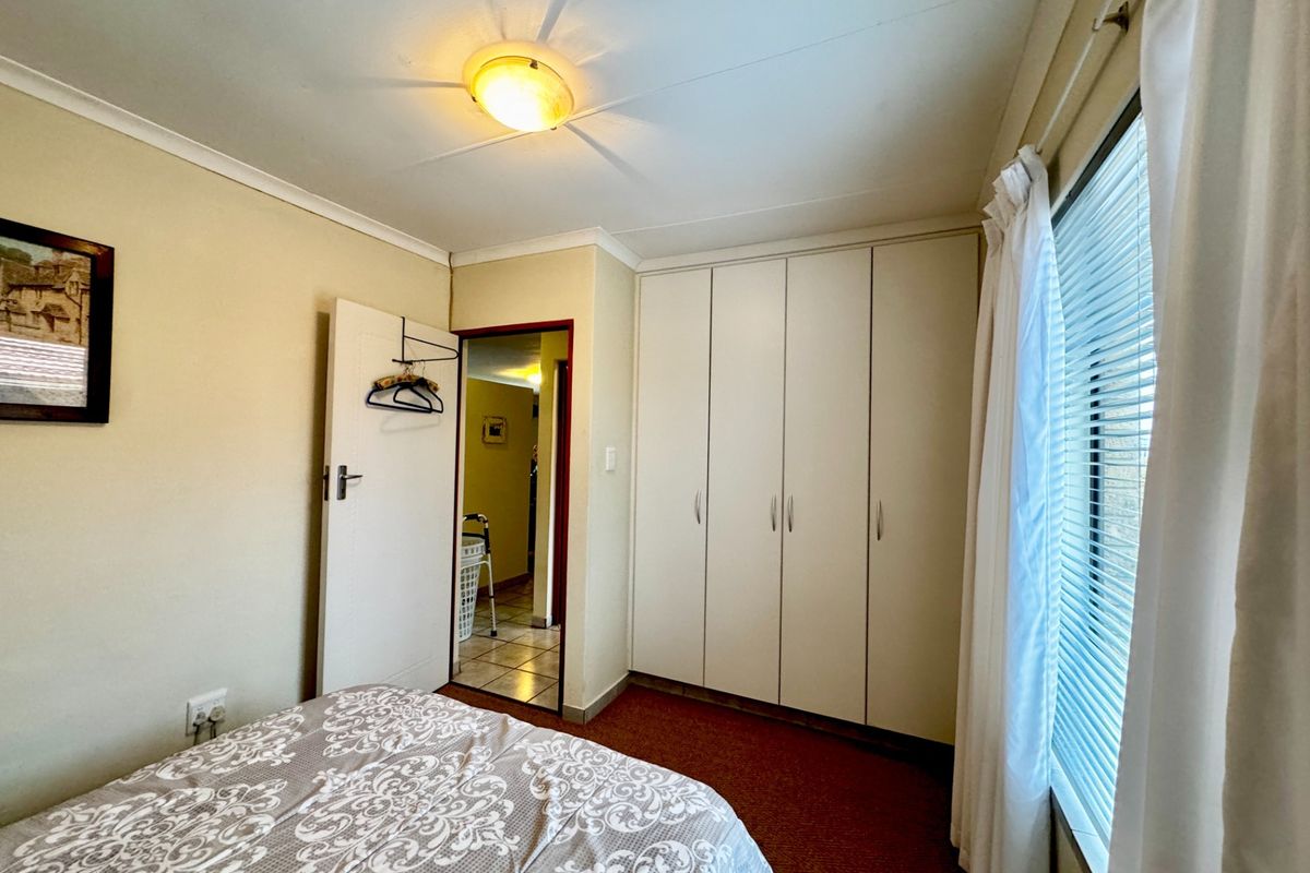 A functional bedroom featuring built-in cupboards, venetian blinds, and neutral wall finishes, providing a practical and comfortable living space.