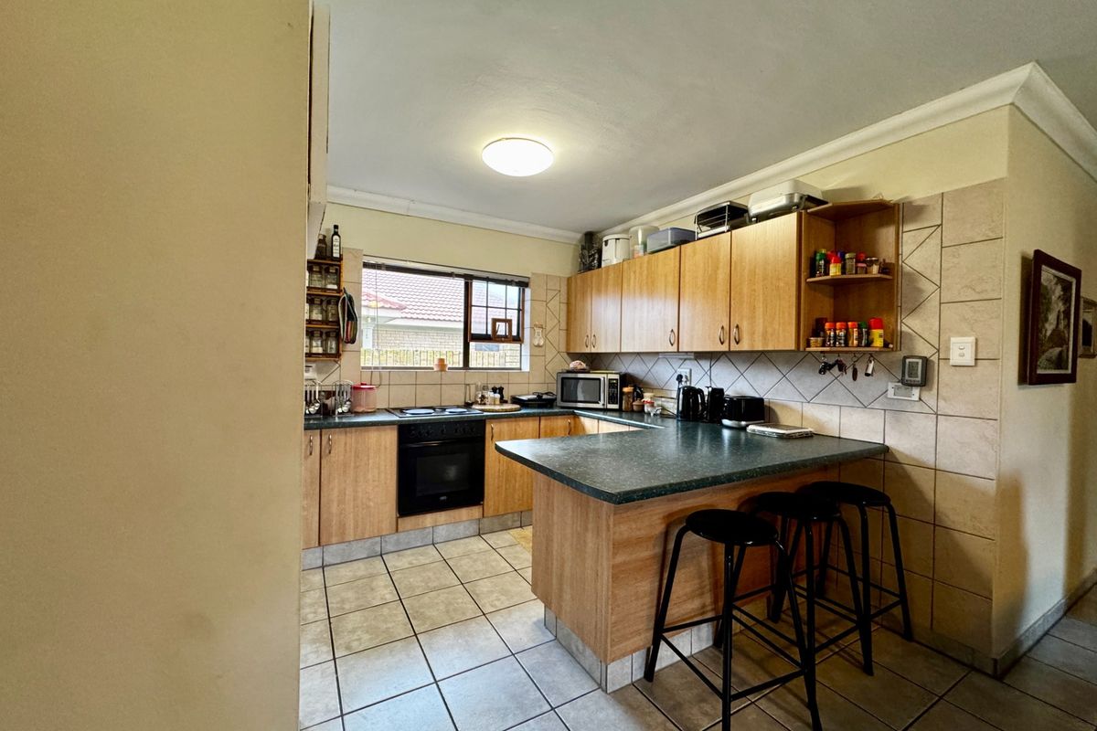 A functional kitchen featuring laminate cabinetry, tiled backsplash, built-in oven, electric hob, and a breakfast bar with tiled flooring.